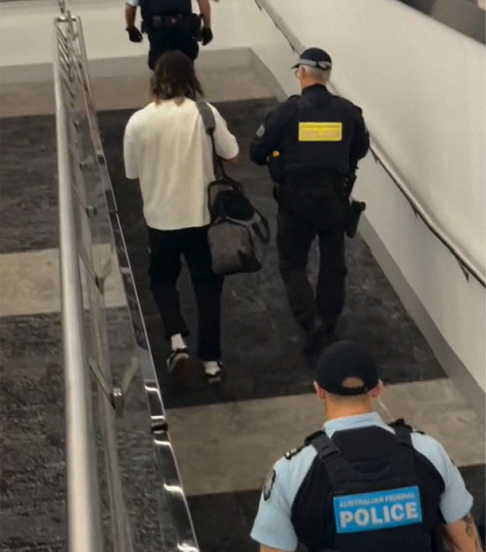 Influencer Hugh Lovett escorted by police officers at an airport following a plane safety demo incident.
