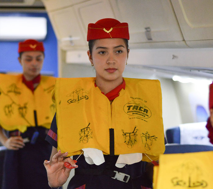 Flight attendant demonstrating how to wear a life vest correctly during an official plane safety demo.