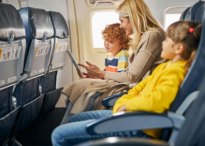 A mother and two children seated in an airplane cabin before a plane safety demo.