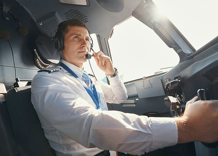 An airline pilot in the cockpit wearing a headset during a flight.