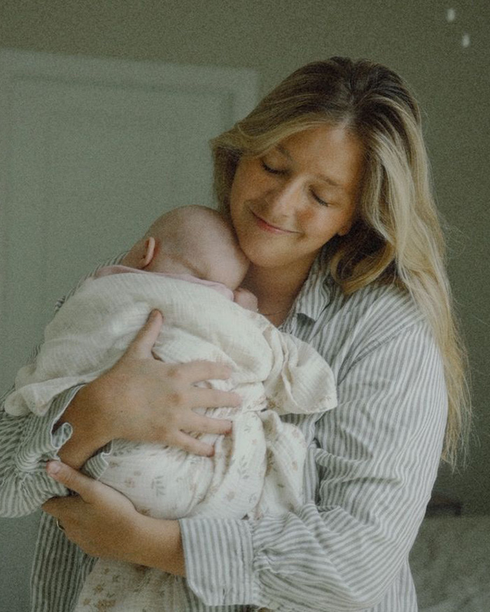 A mom holding her baby closely in a neutral, muted beige-toned room. A mom holding her baby closely in a neutral, muted beige-toned room.