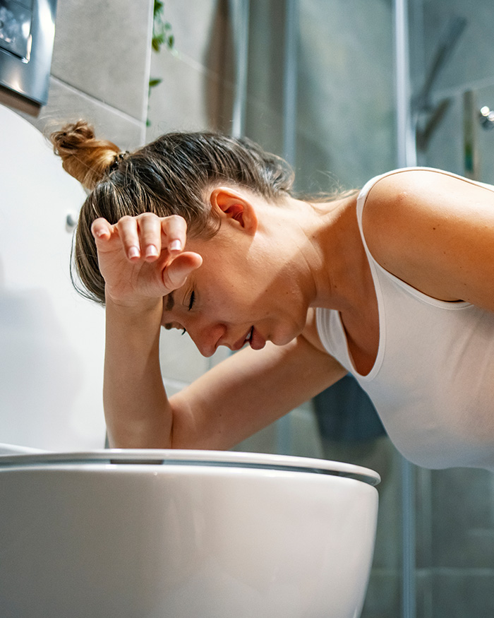 Woman leaning over a toilet suffering from food poisoning after eating sushi.