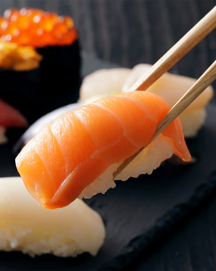 Chopsticks holding fresh salmon nigiri sushi over a platter highlighting eating sushi risks.