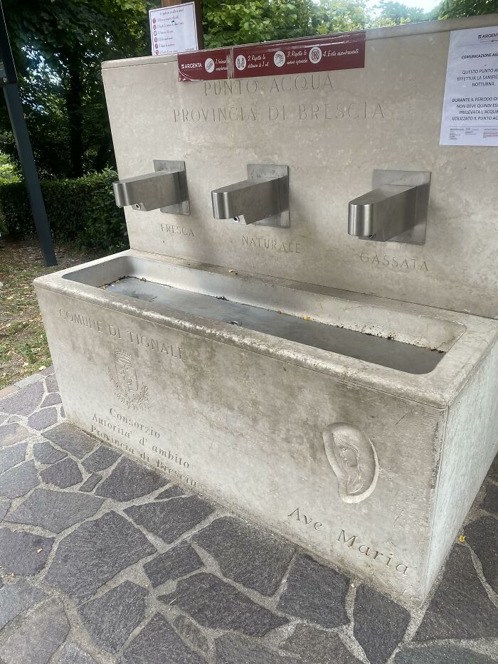 Public stone drinking fountain with three metal taps in Brescia, Italy, showcasing useful and ingenious things.