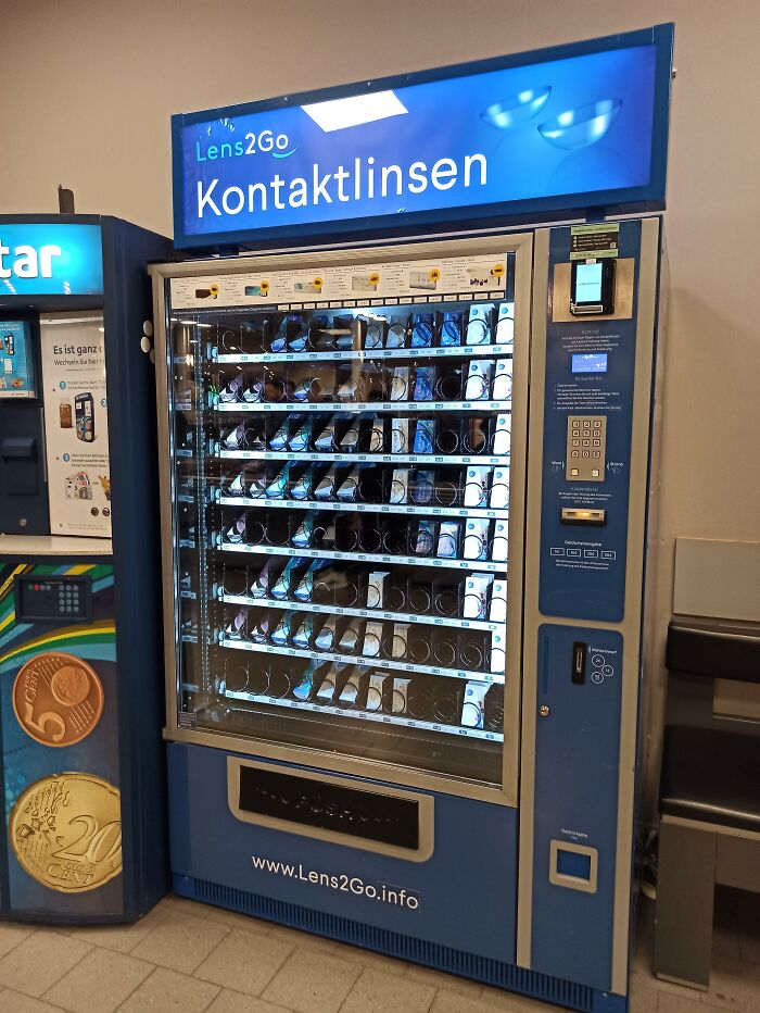 Blue contact lens vending machine with German text standing indoors, showing useful and ingenious things.