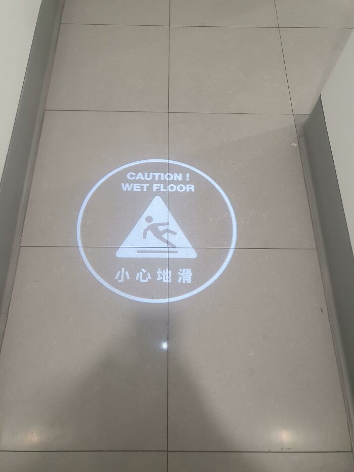 A projected wet floor warning sign on tiled flooring, showcasing ingenious things in various parts of the world.