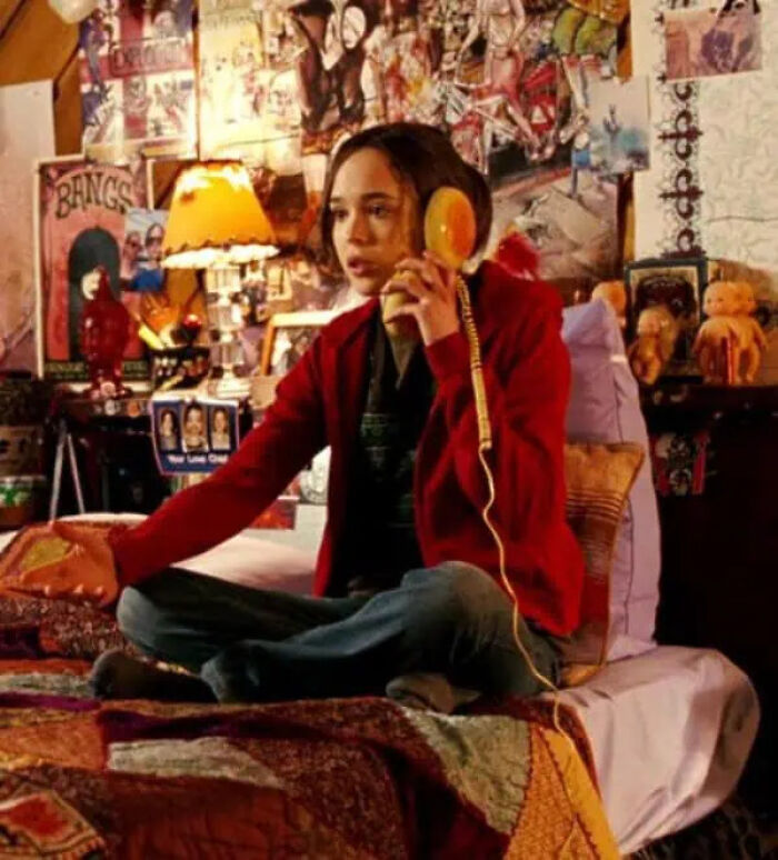 A movie character sitting cross-legged on a bed, talking on a hamburger phone prop