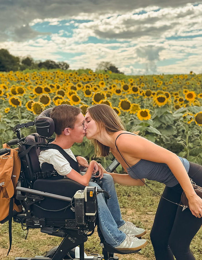 Interabled couple kisses in a sunflower field celebrating their new pregnancy journey.