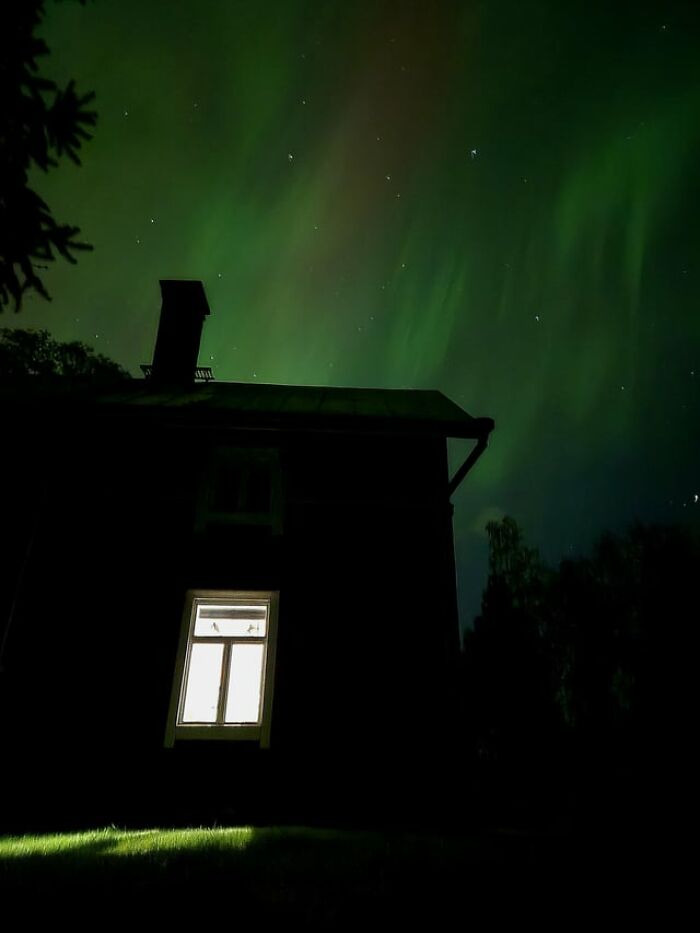 Silhouette of a house illuminated by glowing green aurora borealis creating creepy photos vibes