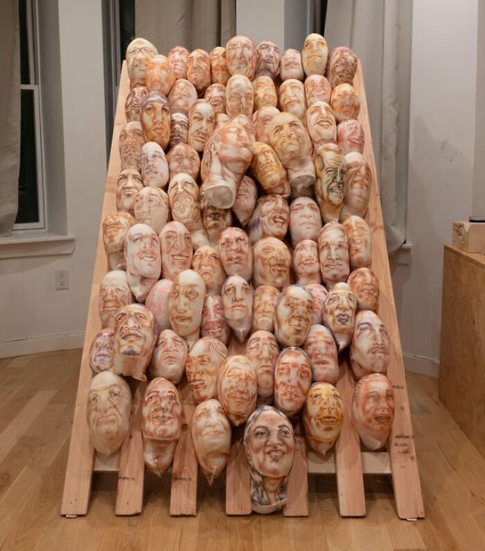 An installation of uncanny ceramic faces arranged on a wooden frame, giving a creepy photo vibe.