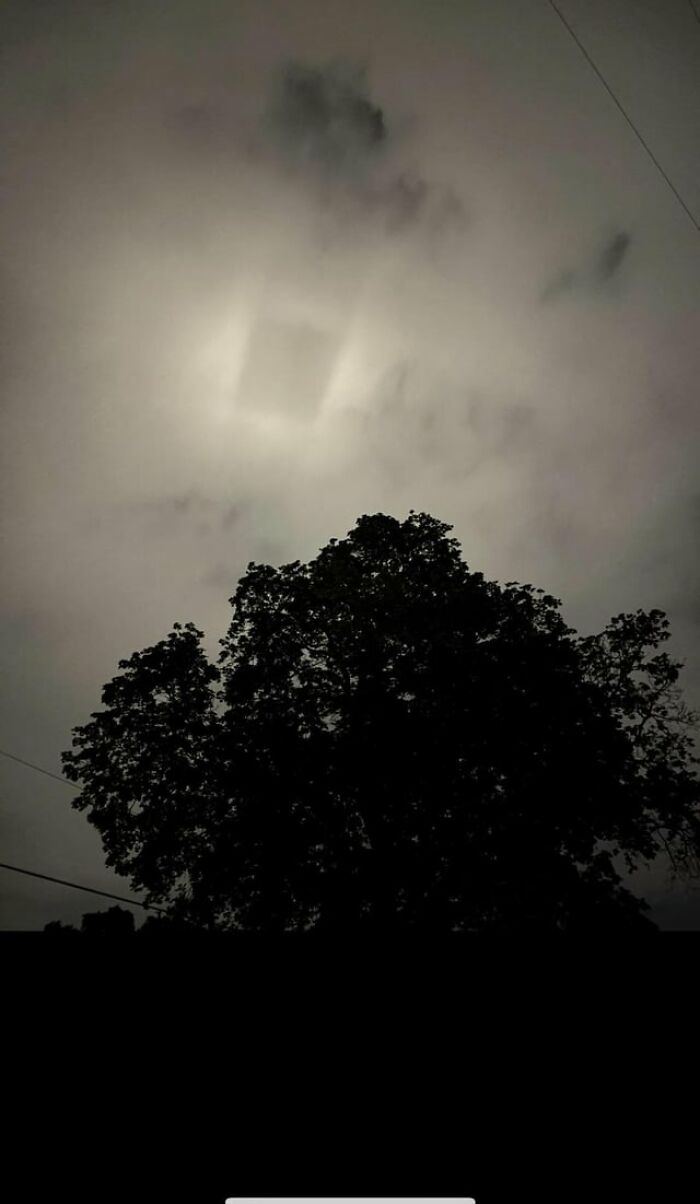 A weird and creepy photo of a strange, square-shaped glowing light in the cloudy night sky.