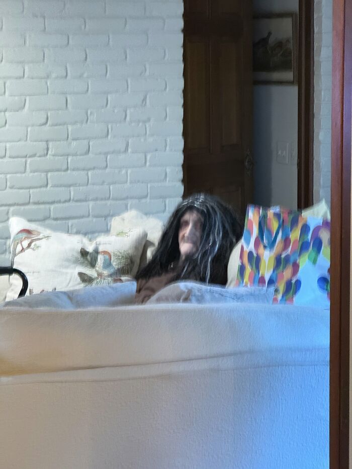 An eerie figure wearing a long black wig sitting on a couch, creating creepy photos.