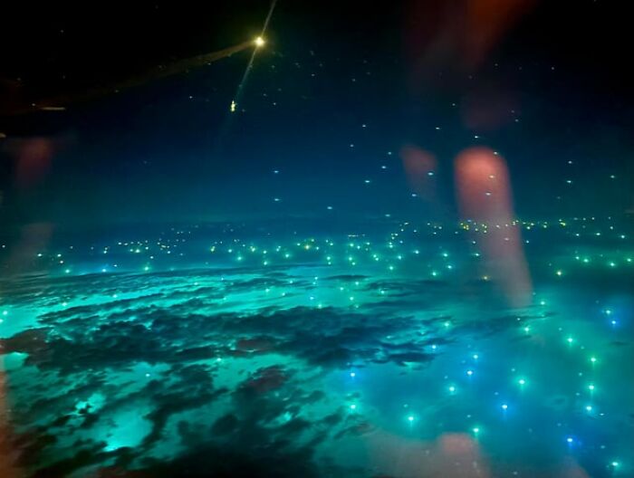 Weird and creepy photos showing a glowing cyan ocean viewed from an airplane window at night.