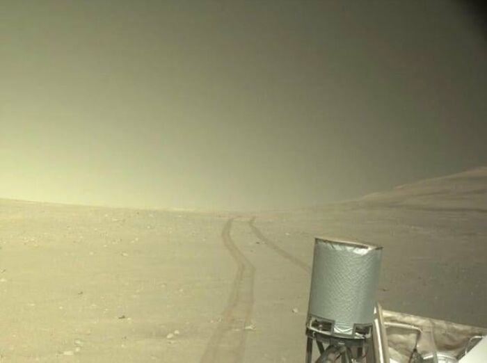 A slightly creepy photo of tracks leading across a desolate, hazy landscape on Mars