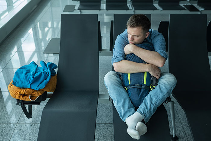Anxious man hugging backpack in airport terminal illustrating worst-case scenario