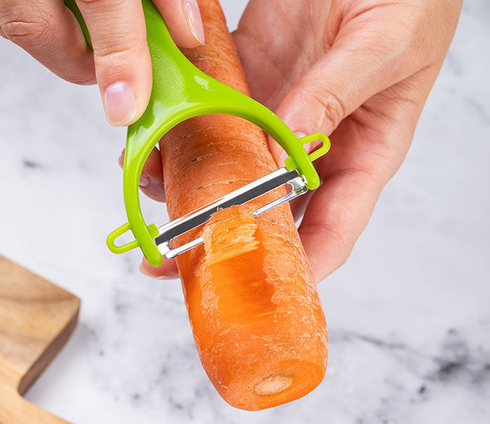 Hands use a peeler on a fresh carrot during a worst-case scenario kitchen moment.