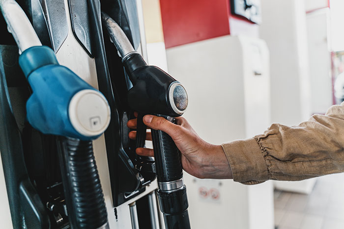 Hand holding a fuel pump nozzle at a gas station amidst worst-case scenarios.