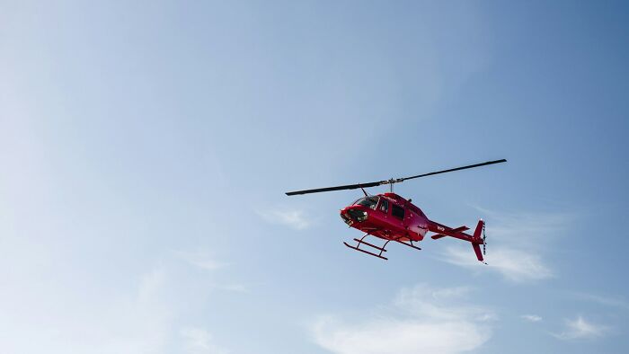 A red helicopter flying high in the blue sky, referencing Hollywood movie tropes.