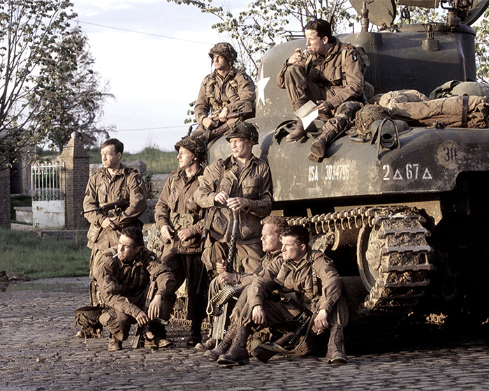 Group of World War II soldiers posing with a military tank on a cobblestone road Group of World War II soldiers posing with a military tank on a cobblestone road
