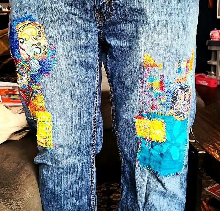 Blue jeans repaired with colorful patterned fabric patches showcasing creativity.