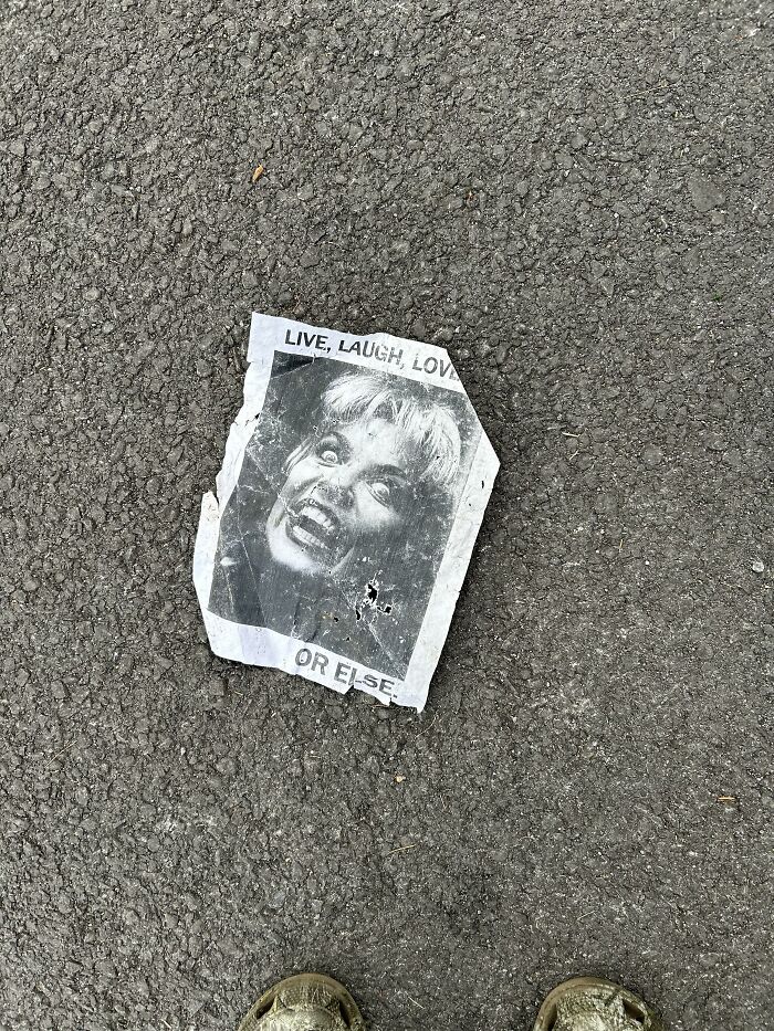 A crumpled paper flyer on asphalt reading Live, Laugh, Love OR ELSE, an example of lost and forgotten messages.