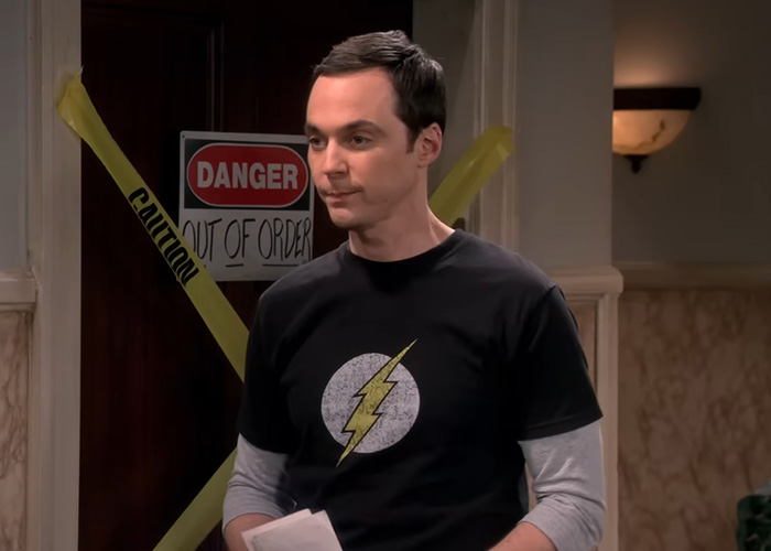 Jim Parsons as Sheldon Cooper wearing a Flash shirt in front of a yellow caution tape. Jim Parsons as Sheldon Cooper wearing a Flash shirt in front of a yellow caution tape.