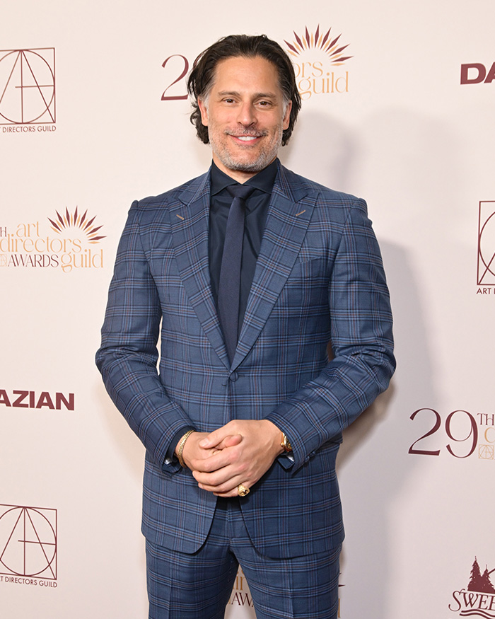 Actor Joe Manganiello posing in a blue plaid suit at an awards ceremony, smiling for the camera.