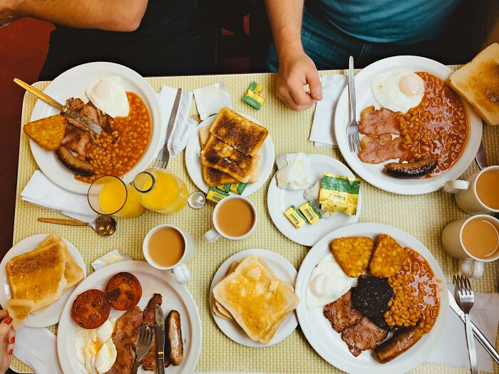 An overhead view of a full English breakfast table, depicting realistic food vs Hollywood movie portions.