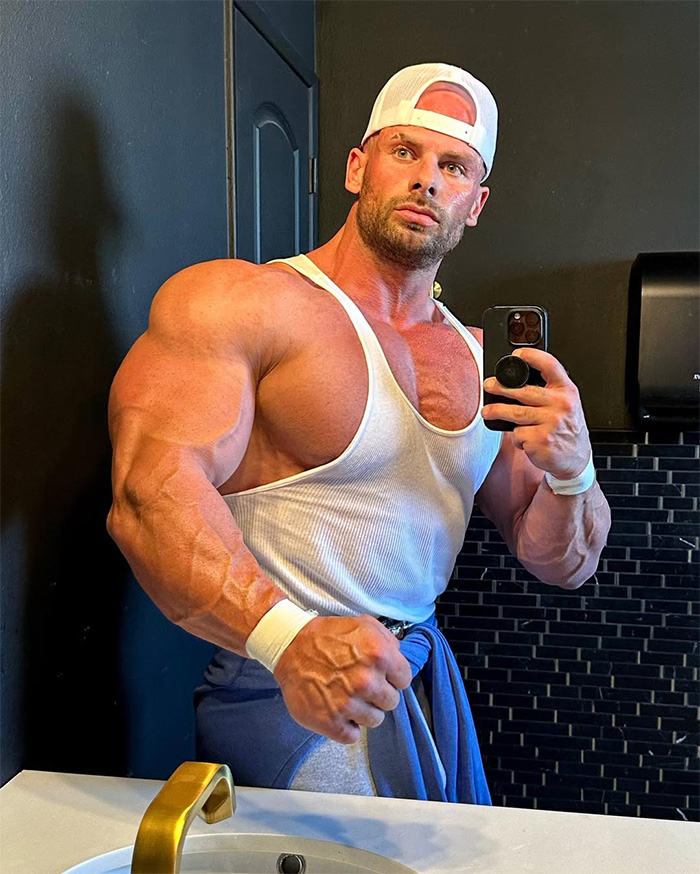 Fitness influencer Joey Swoll posing for a mirror selfie showing his large muscles in a tank top. Fitness influencer Joey Swoll posing for a mirror selfie showing his large muscles in a tank top.