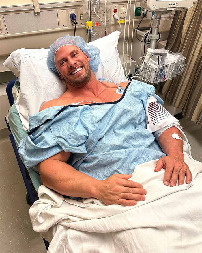 Joey Swoll lying in a hospital bed wearing a hairnet and smiling while recovering from surgery. Joey Swoll lying in a hospital bed wearing a hairnet and smiling while recovering from surgery.