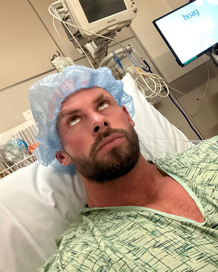 Joey Swoll in a hospital gown and hairnet looking up at medical equipment from a hospital bed. Joey Swoll in a hospital gown and hairnet looking up at medical equipment from a hospital bed.