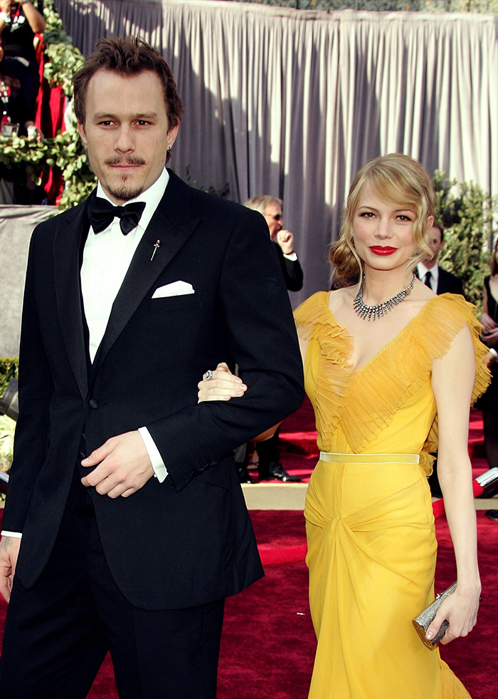 Hollywood actress in a yellow gown walking arm in arm with her late co-star in a tuxedo at a formal event.