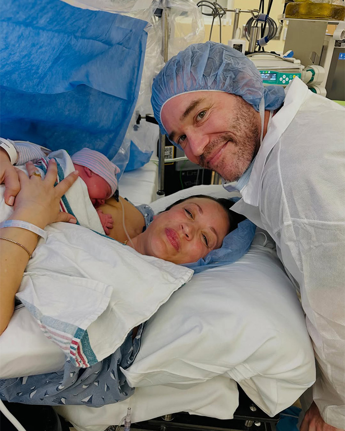 Mother lying in hospital bed holding newborn baby with father in scrubs Mother lying in hospital bed holding newborn baby with father in scrubs