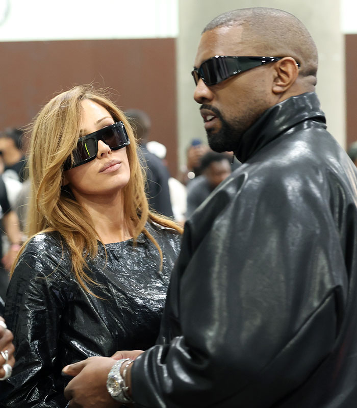 Kanye West and Bianca Censori wearing dark sunglasses while conversing close together.