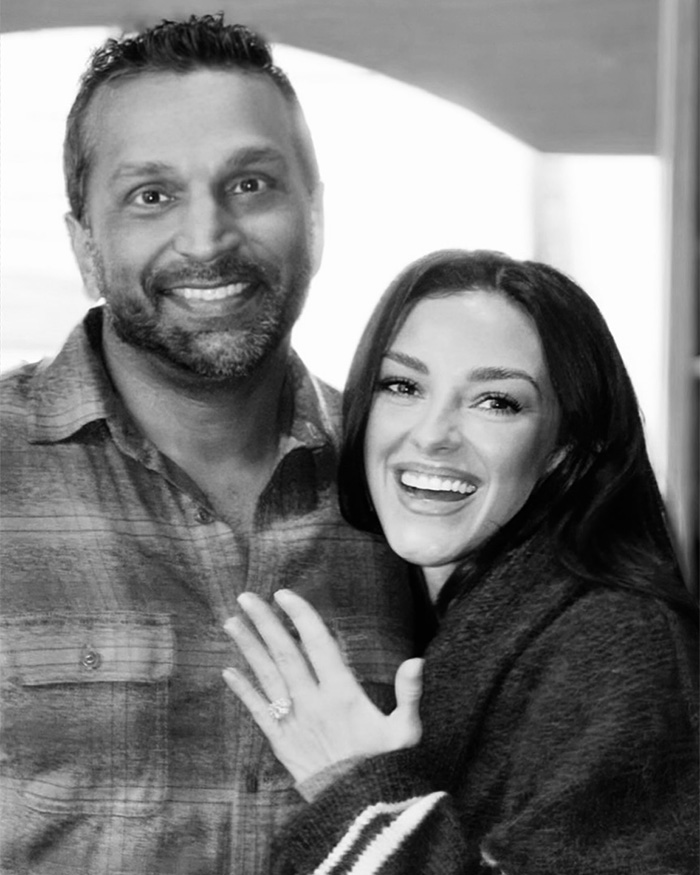 Black and white photo of Kash Patel and his fiance&eacute; smiling as she shows her engagement ring.