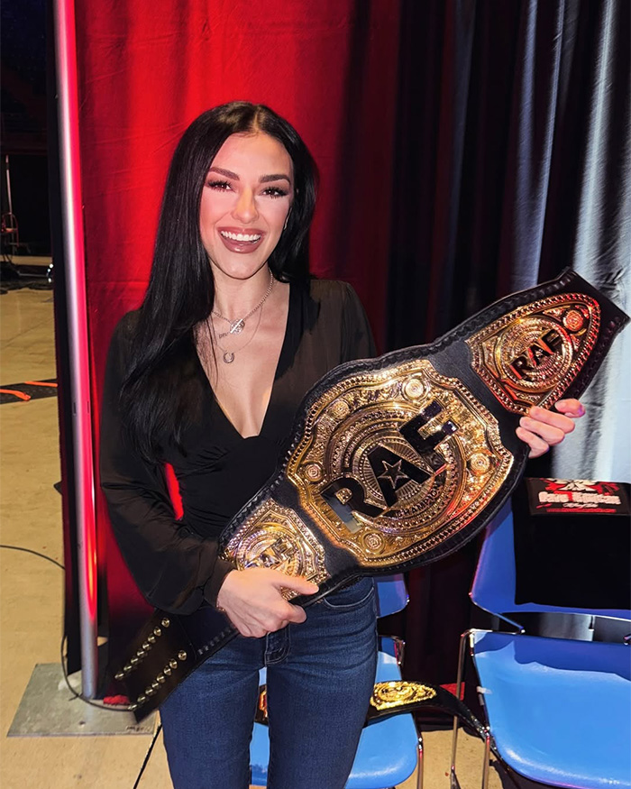 Kash Patel fiance&eacute; holding up a heavy championship belt and smiling