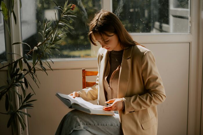 A young professional woman sitting inside and reading a book, representing working with clients