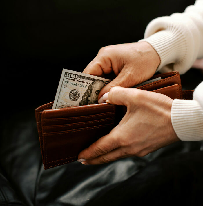 Person placing hundred dollar bill in brown leather wallet showing wealth