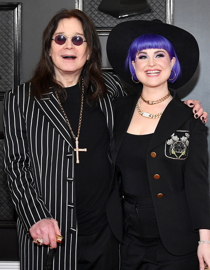 Kelly Osbourne with purple hair smiling next to Ozzy Osbourne on the red carpet.