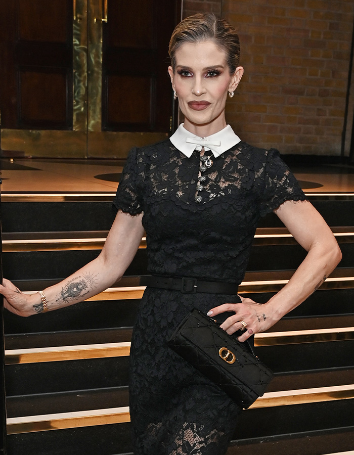 Kelly Osbourne wearing a black lace dress with a white collar posing on steps.