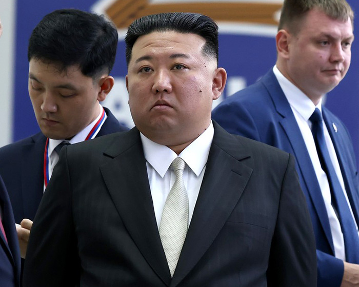 Kim Jong Un standing in a dark suit surrounded by officials. Kim Jong Un standing in a dark suit surrounded by officials.