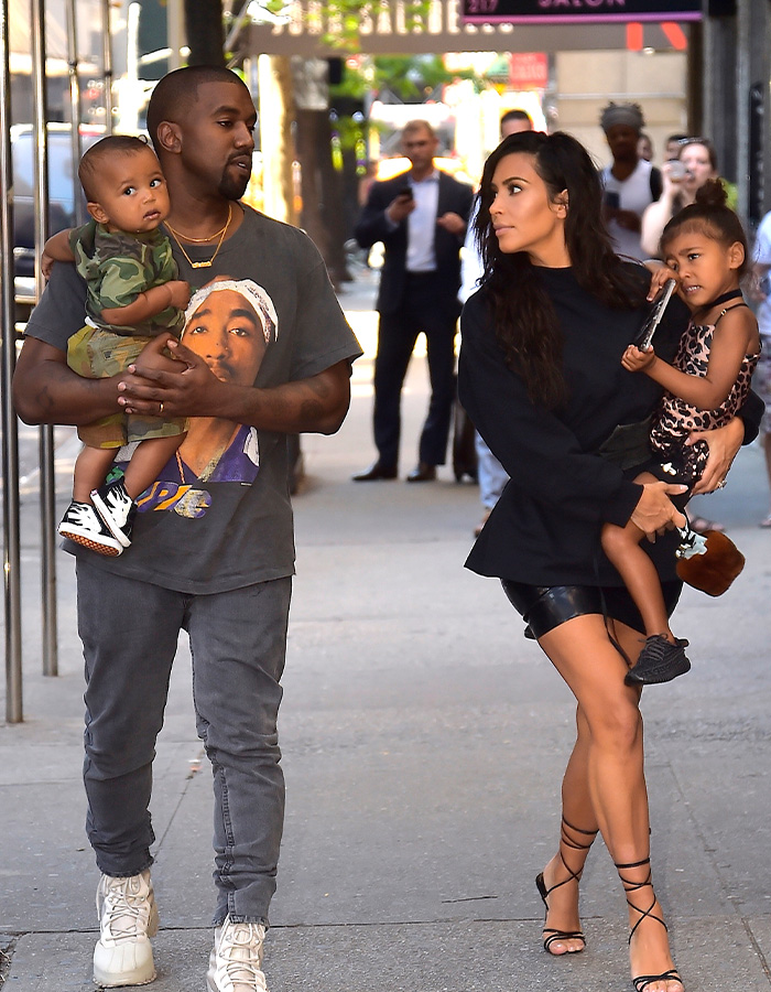 Kim Kardashian and Kanye West walking on a city street while carrying two of their 4 kids Kim Kardashian and Kanye West walking on a city street while carrying two of their 4 kids