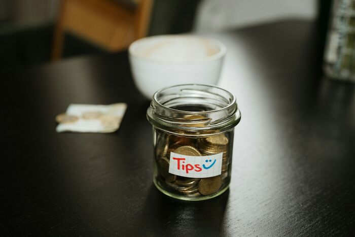 Tip jar filled with coins on cafe table closeup