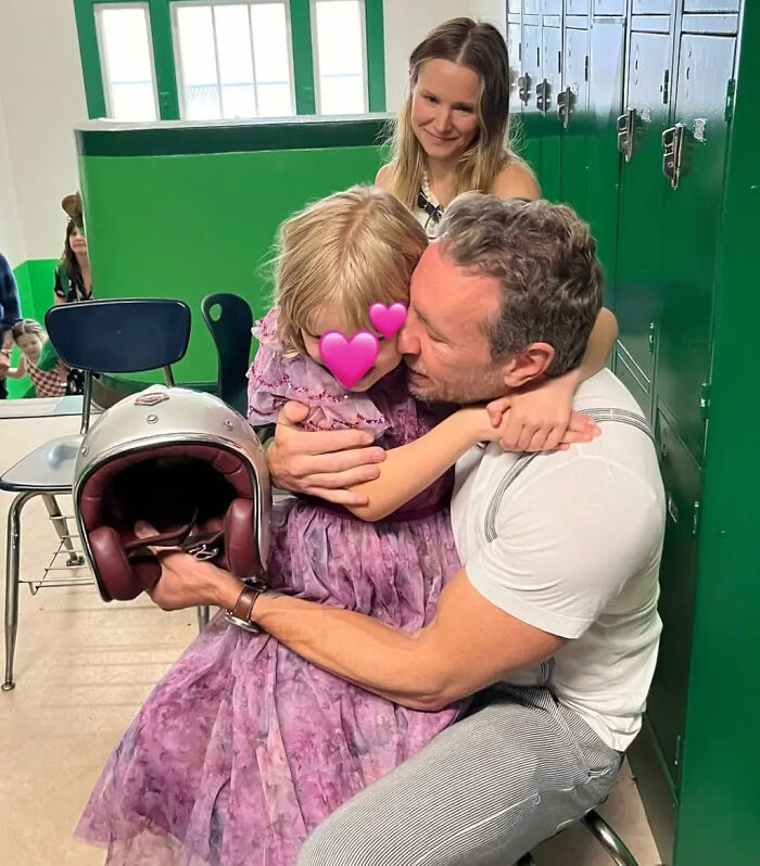 Kristen Bell and Dax Shepard hugging child with heart emojis over face while sitting in front of green lockers