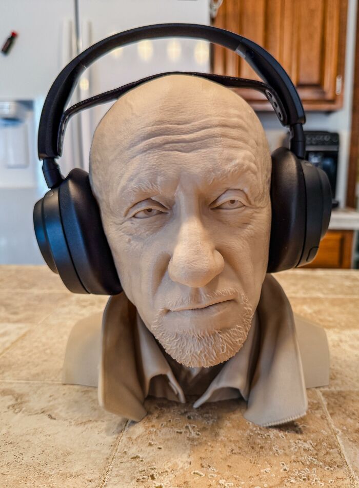 A realistic 3D prints head sculpture of an older man wearing headphones.