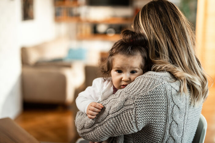 A worried little child looking over their mother's shoulder.