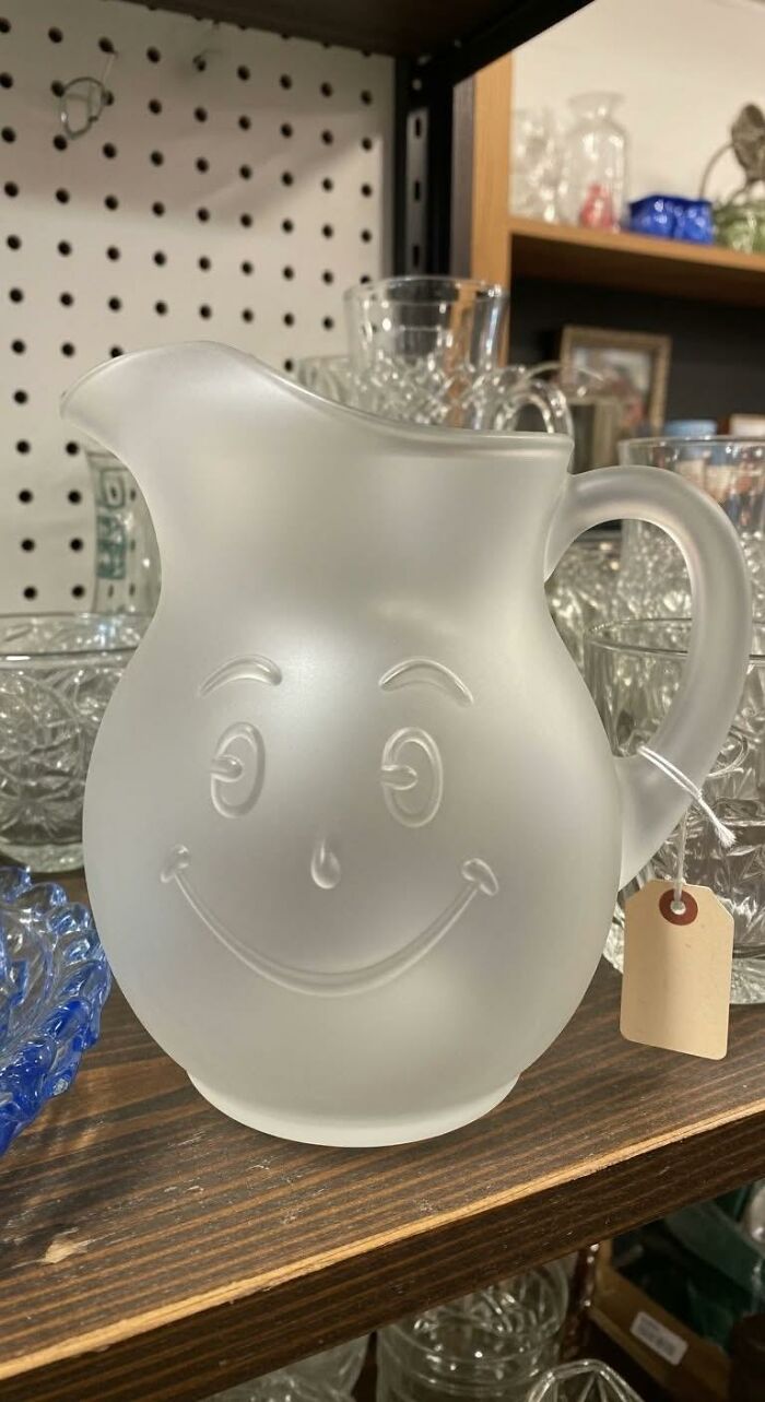 Frosted glass Kool-Aid pitcher sitting on a wooden shelf, a iconic piece of '80s kids nostalgia.