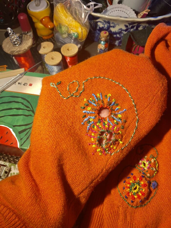 Bright orange sweater repaired with colorful embroidery, displaying creativity to save money on clothes.