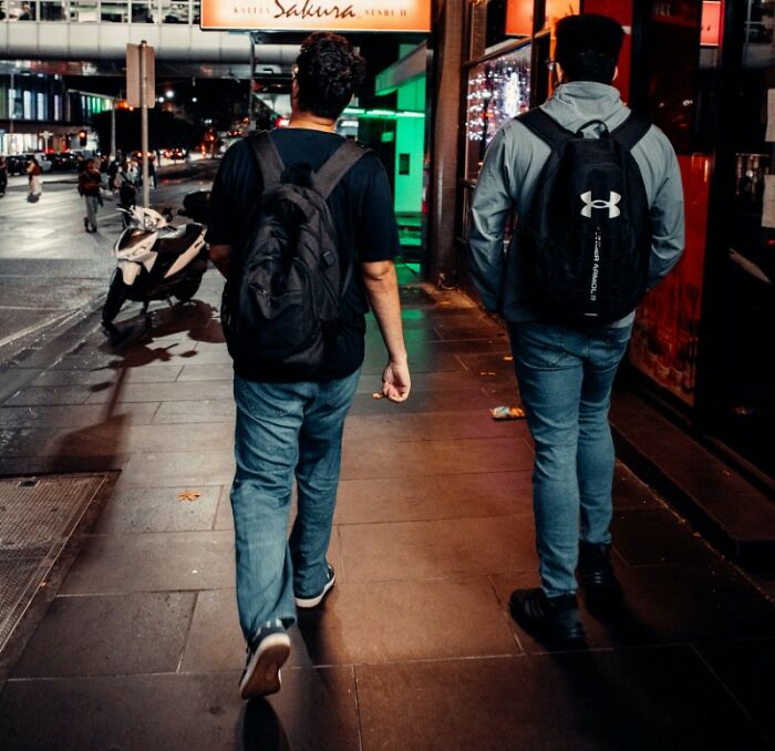Two young men with backpacks walking down a city street at night, following a gut feeling.