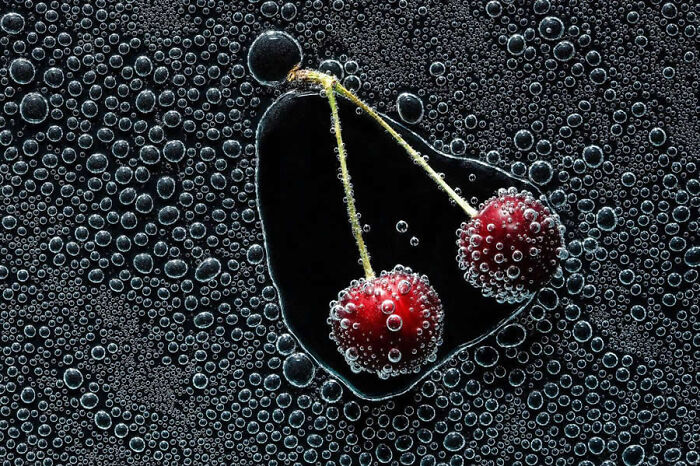 Stunning macro photo of two cherries submerged in water surrounded by fine bubbles.